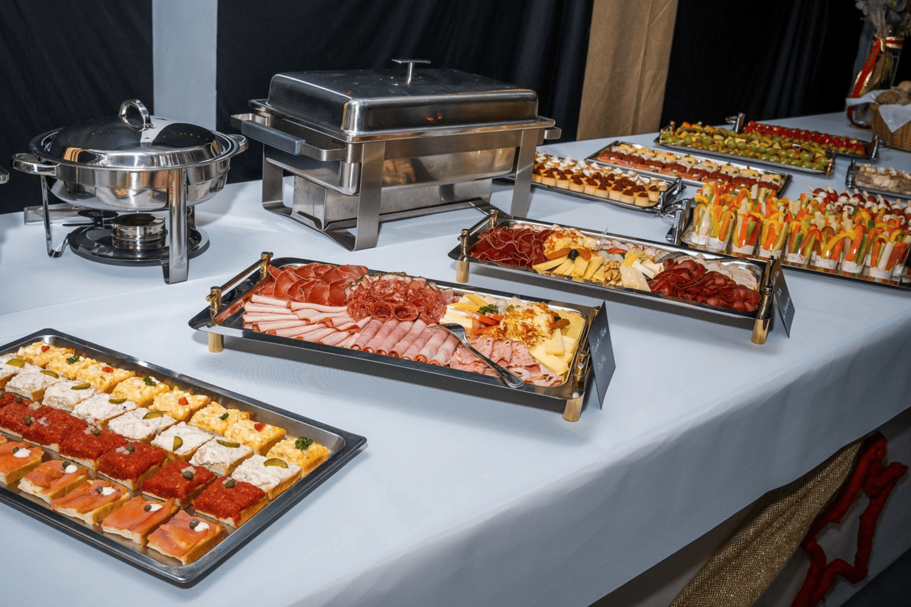 Ein Buffet von Metzgerei Koller in Sirnach mit Warmhaltebehältern und verschiedenen Platten mit aufgeschnittenem Fleisch, Käse und Vorspeisen auf einer weißen Tischdecke.