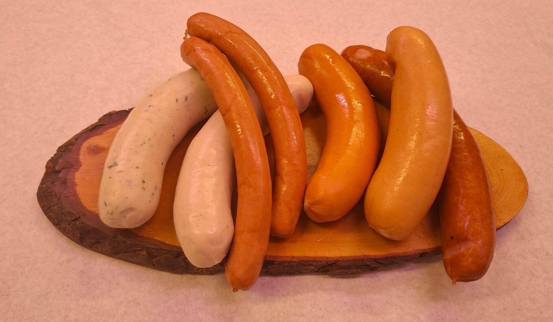 Eine Auswahl verschiedener Wurstsorten von Metzgerei Koller in Sirnach, von blassweiß bis rötlich-braun, auf einem Holzbrett angerichtet.