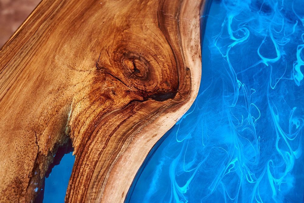 Holztisch mit einem Fluss aus durchscheinendem, leuchtend blauem Epoxidharz.