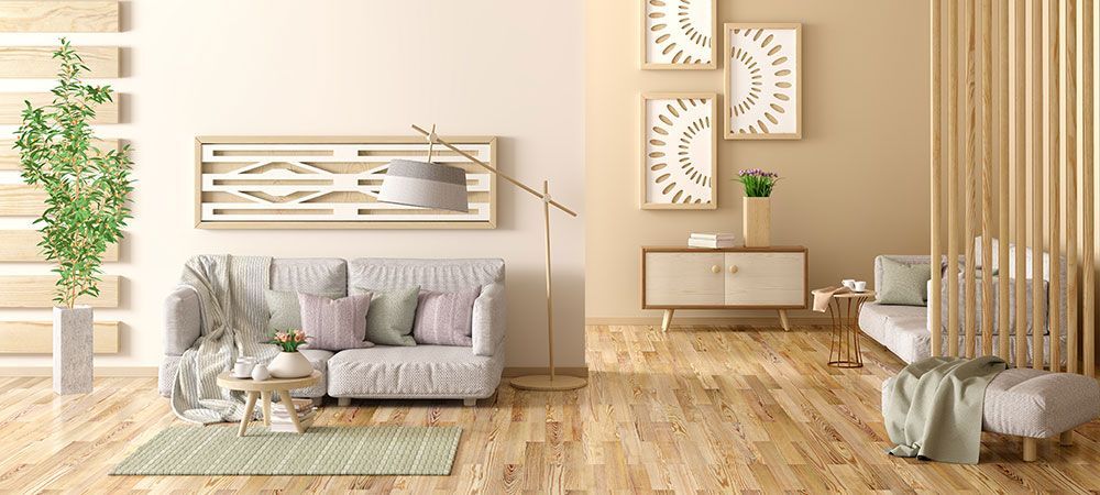 Gemütliches Wohnzimmer mit hellen Holzböden, beigen Wänden, hellgrauem Sofa, grünem Teppich und dekorativen Uhren.