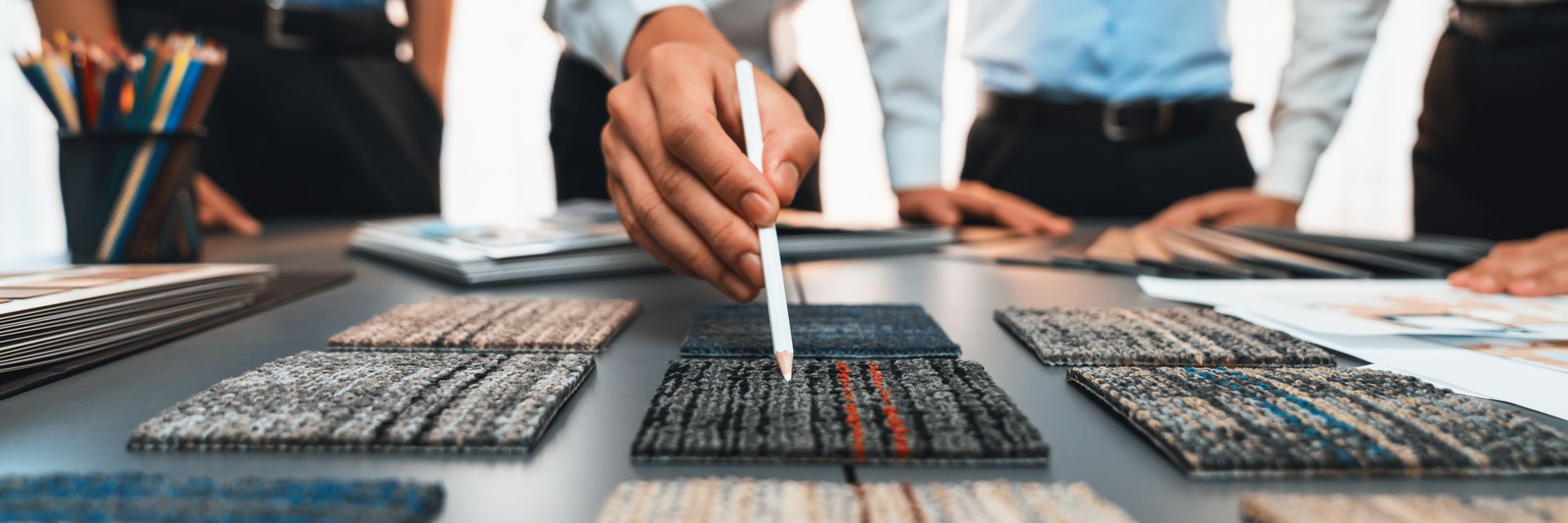 Eine Person zeigt mit anderen an einem Tisch auf Teppichmuster.