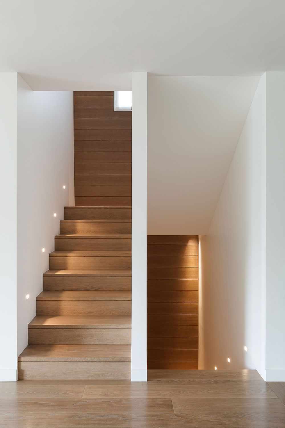 Holztreppe mit Einbauleuchten in einem modernen weißen Flur.
