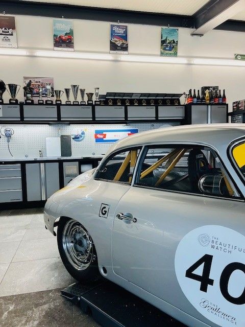 Voiture de course argentée dans un garage avec des étagères à trophées et des affiches de course ; numéro 40 sur la portière.