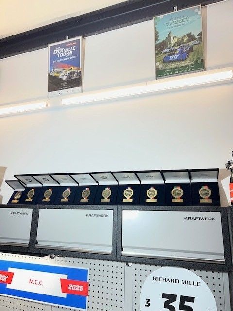 Étagère d'exposition avec médaillons encadrés dans des boîtes, affiches au-dessus et étiquettes de prix.