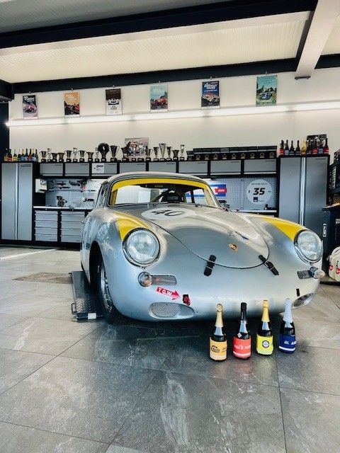 Une Porsche de course vintage argentée dans un garage avec des bouteilles devant.