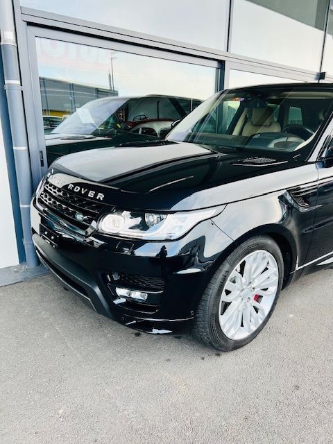 Un SUV Range Rover noir est garé à l'extérieur, avec une voiture verte partiellement visible en arrière-plan.