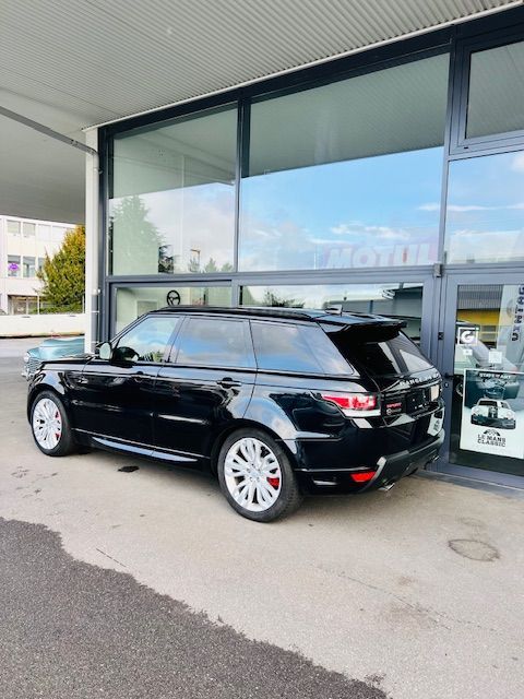 Un Range Rover Sport noir est garé devant un bâtiment aux fenêtres vitrées. Jantes blanches, étriers de freins rouges.