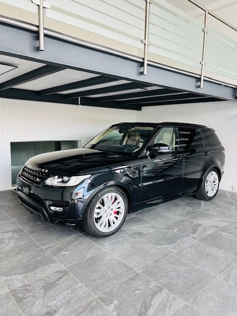 Un SUV Range Rover Sport noir est garé dans un garage moderne avec un sol carrelé gris et un plafond blanc.