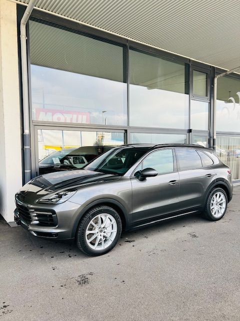 Un SUV Porsche gris est garé devant un immeuble aux grandes fenêtres.