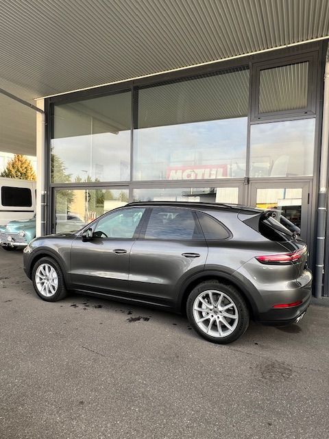 Un SUV Porsche gris est garé devant un immeuble aux grandes fenêtres.