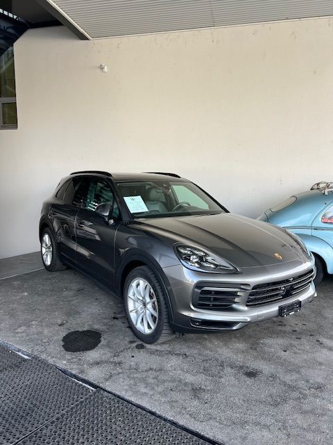 Un SUV Porsche gris foncé est garé à l'intérieur. Une voiture classique bleu clair est partiellement visible sur la droite.