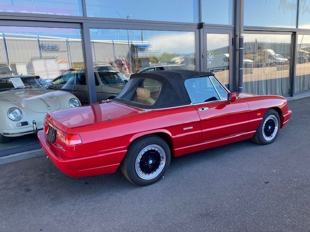 Une Alfa Romeo Spider décapotable rouge garée devant un bâtiment aux fenêtres vitrées.