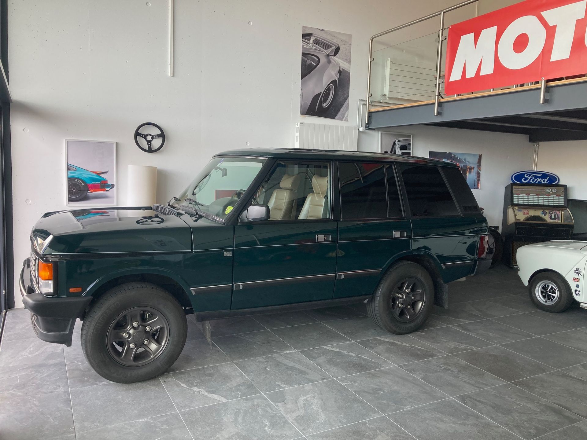 Un Range Rover vert foncé est garé dans un garage avec une mezzanine et des posters.