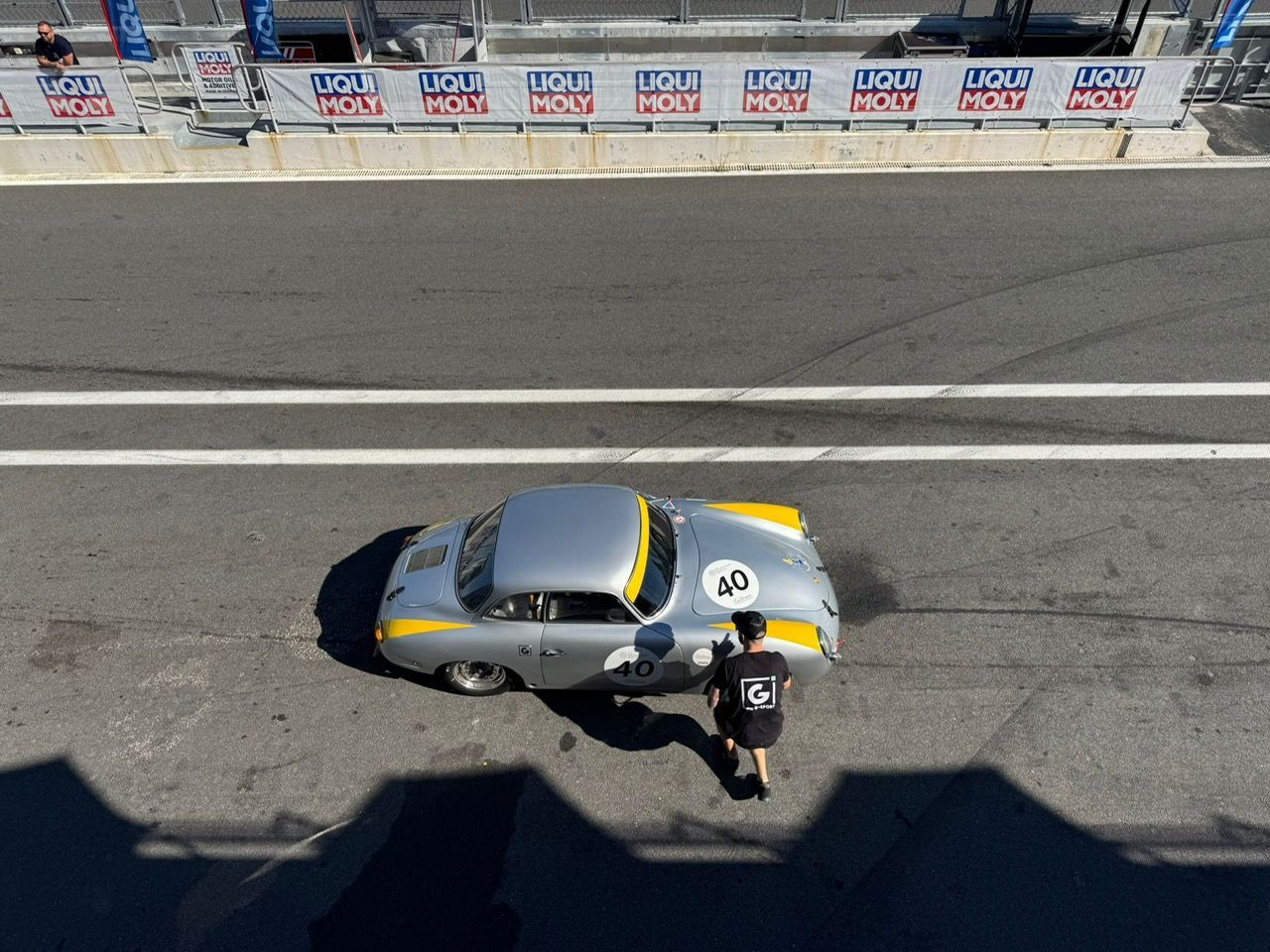 Voiture de sport argentée avec des touches de jaune en cours d'entretien sur un circuit ; un mécanicien fait le plein.