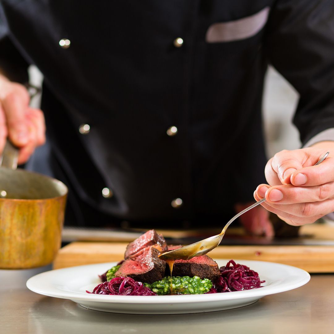 Ein Koch bereitet einen Teller mit Essen mit einem Löffel zu