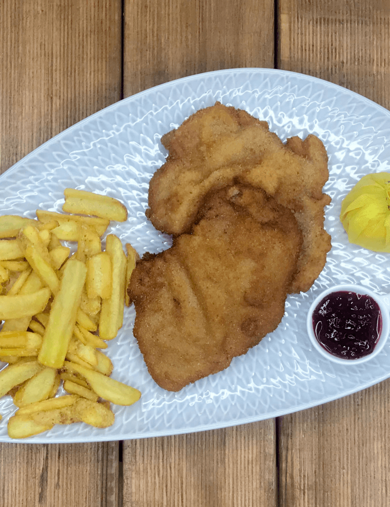 Ein weißer Teller mit gebratenem Hühnchen und Pommes Frites auf einem Holztisch.