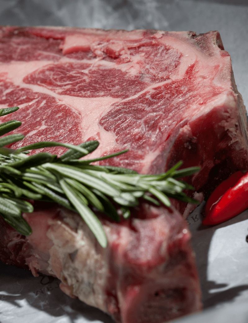 Ein Stück rohes Fleisch mit Rosmarin und einer roten Paprika auf einem Teller.