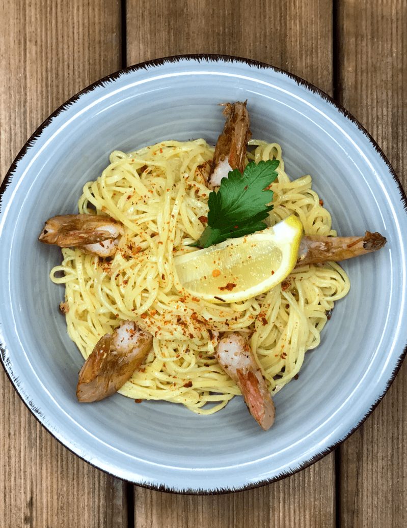 Eine Schüssel Nudeln mit Garnelen und einer Zitronenscheibe auf einem Holztisch.