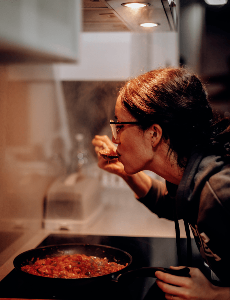 Eine Frau trägt eine Brille und isst Essen aus einer Pfanne auf dem Herd.