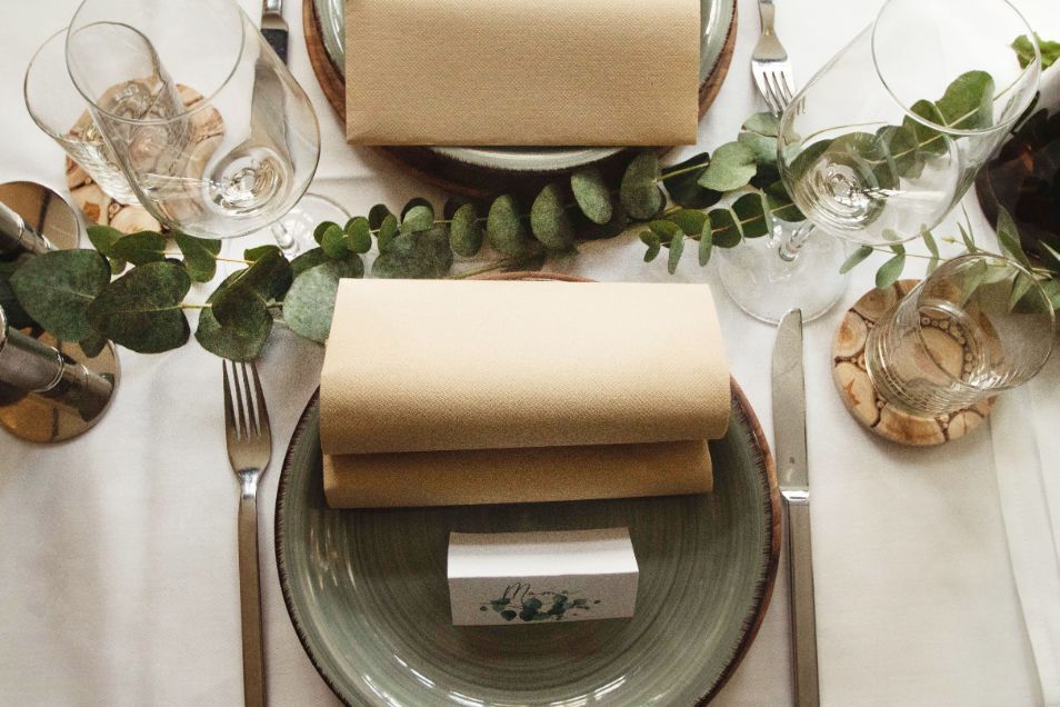 Ein gedeckter Tisch mit Tellern, Servietten, Besteck und Gläsern.