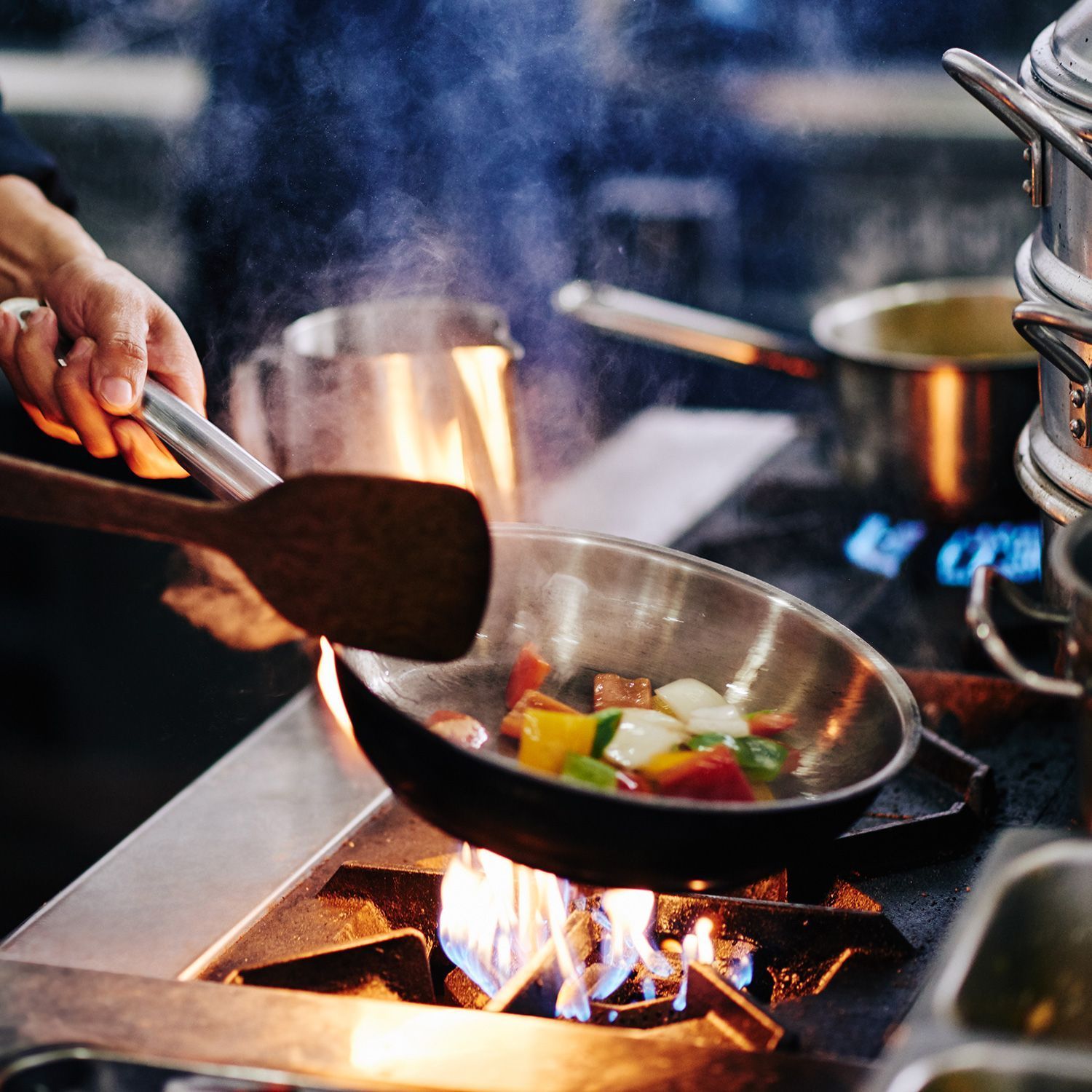 Eine Person rührt Gemüse in einer Bratpfanne auf einem Herd