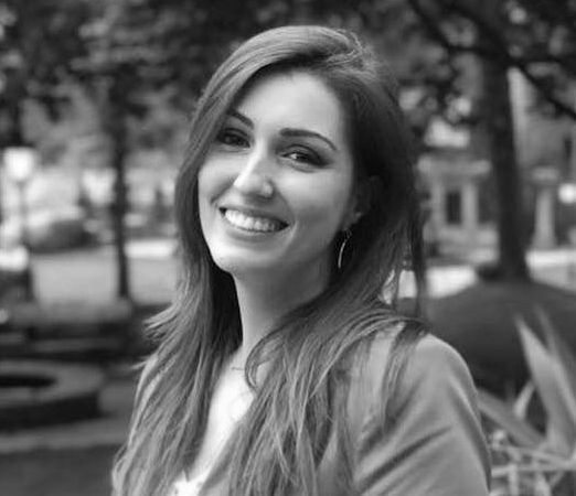 Mujer con cabello largo sonríe al aire libre en blanco y negro, probablemente un parque.