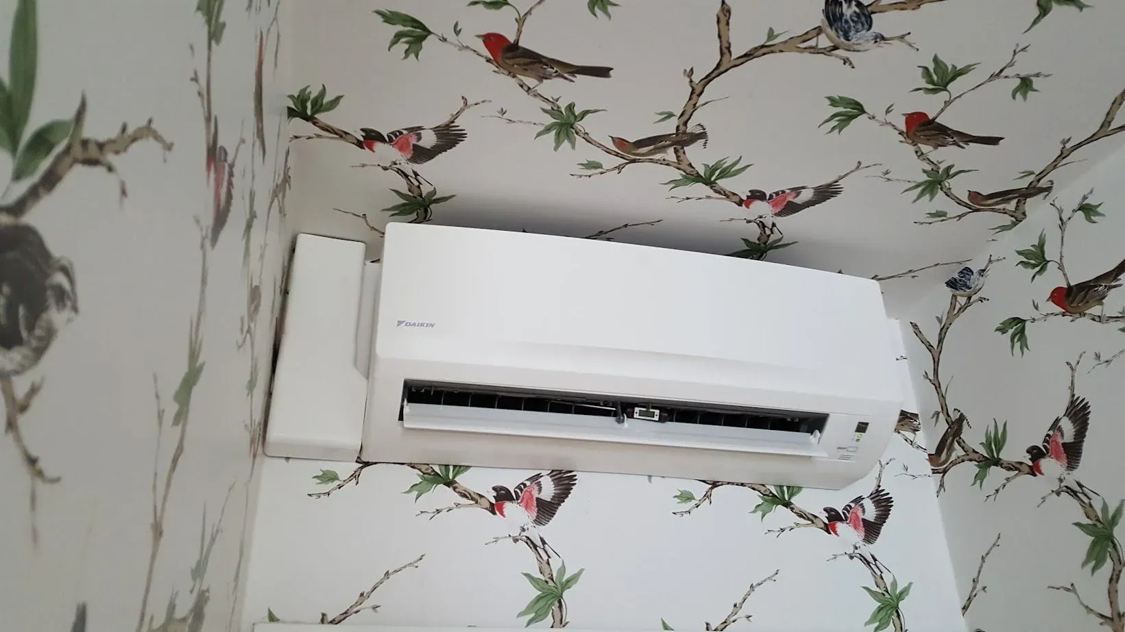 Un acondicionador de aire blanco está colgado en una pared con pájaros en él.