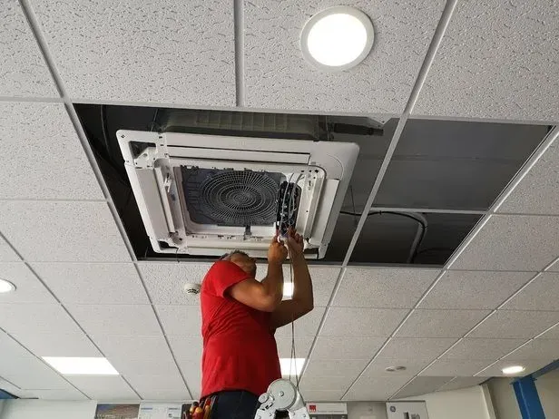 Un hombre con una camisa roja está trabajando en un ventilador de techo.