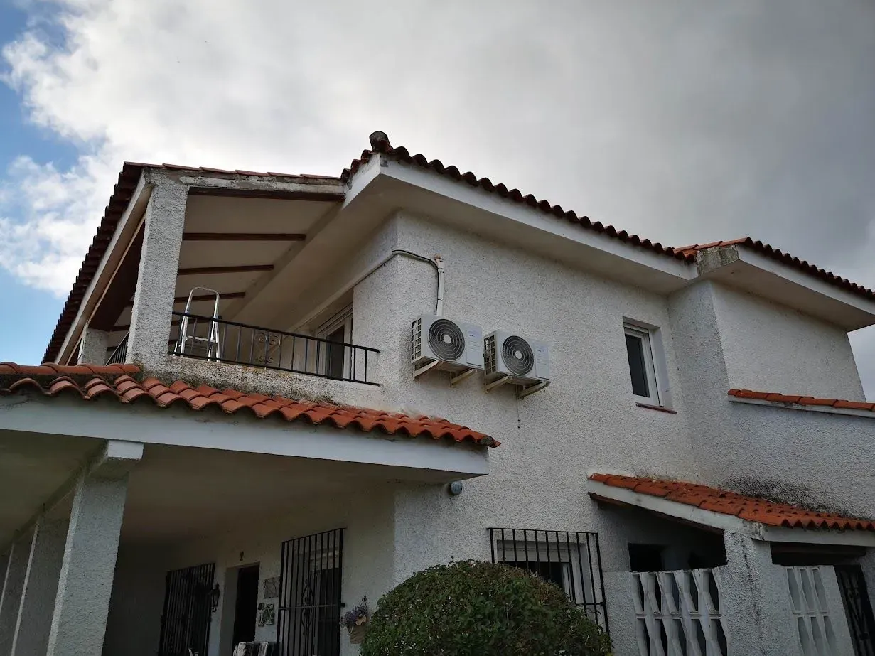 Una casa blanca con techo de tejas rojas y aires acondicionados en los laterales.