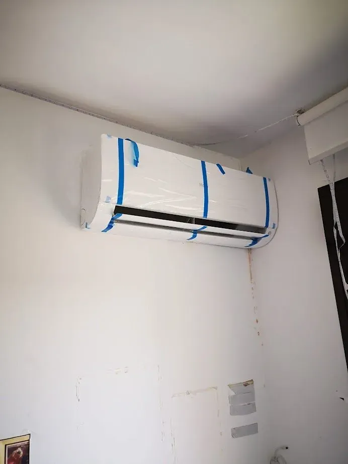 Un acondicionador de aire blanco está pegado a una pared blanca en una habitación.