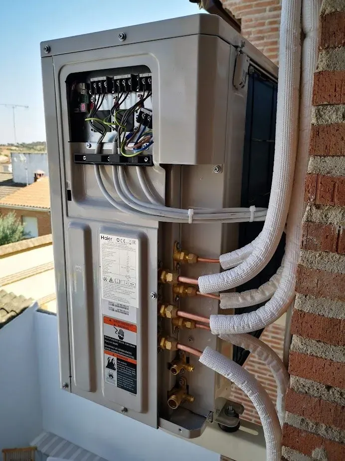 Un acondicionador de aire está colgado en una pared de ladrillos con tubos de cobre conectados a él.