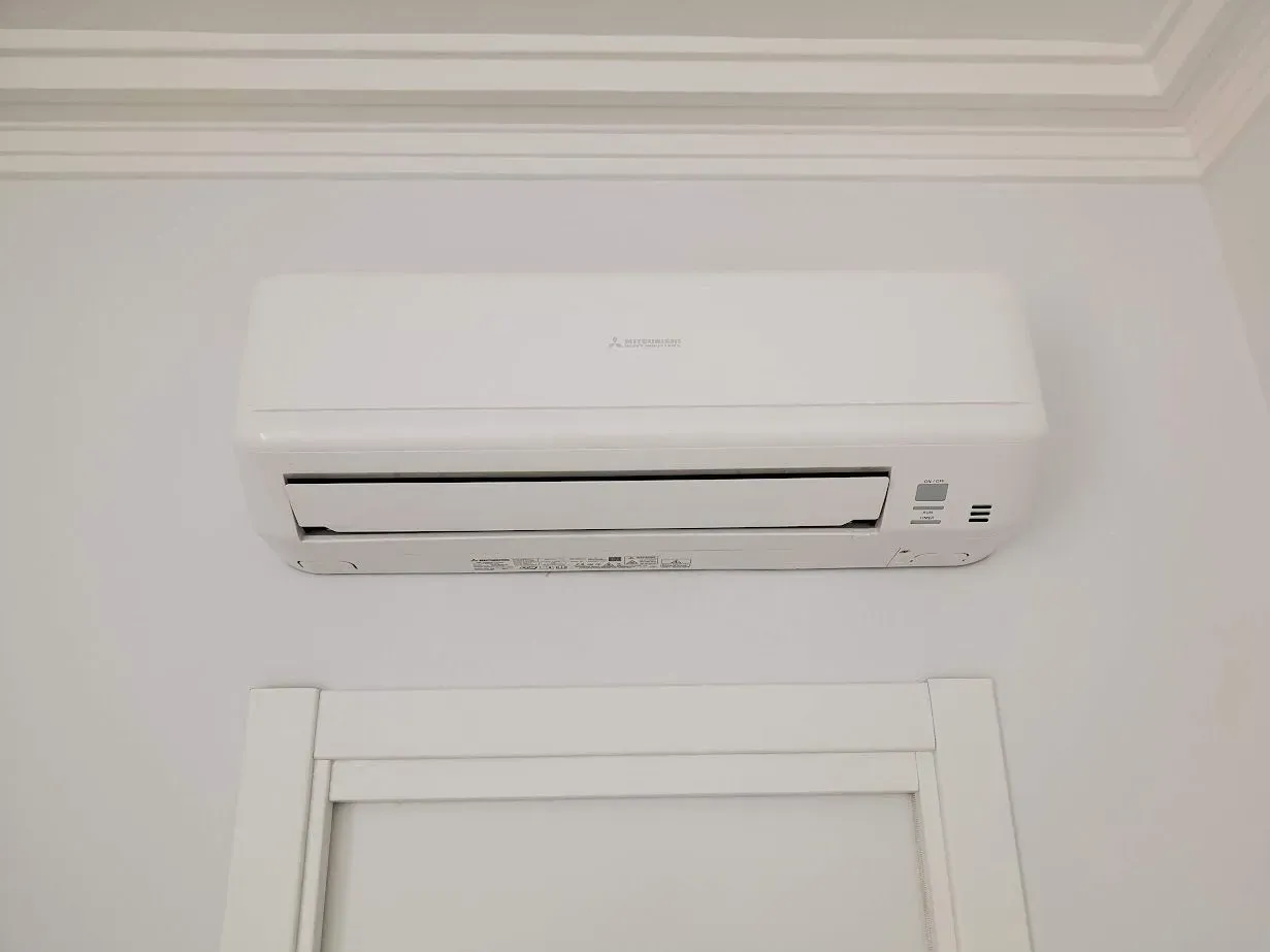 Un acondicionador de aire blanco está colgado en una pared blanca al lado de una puerta.