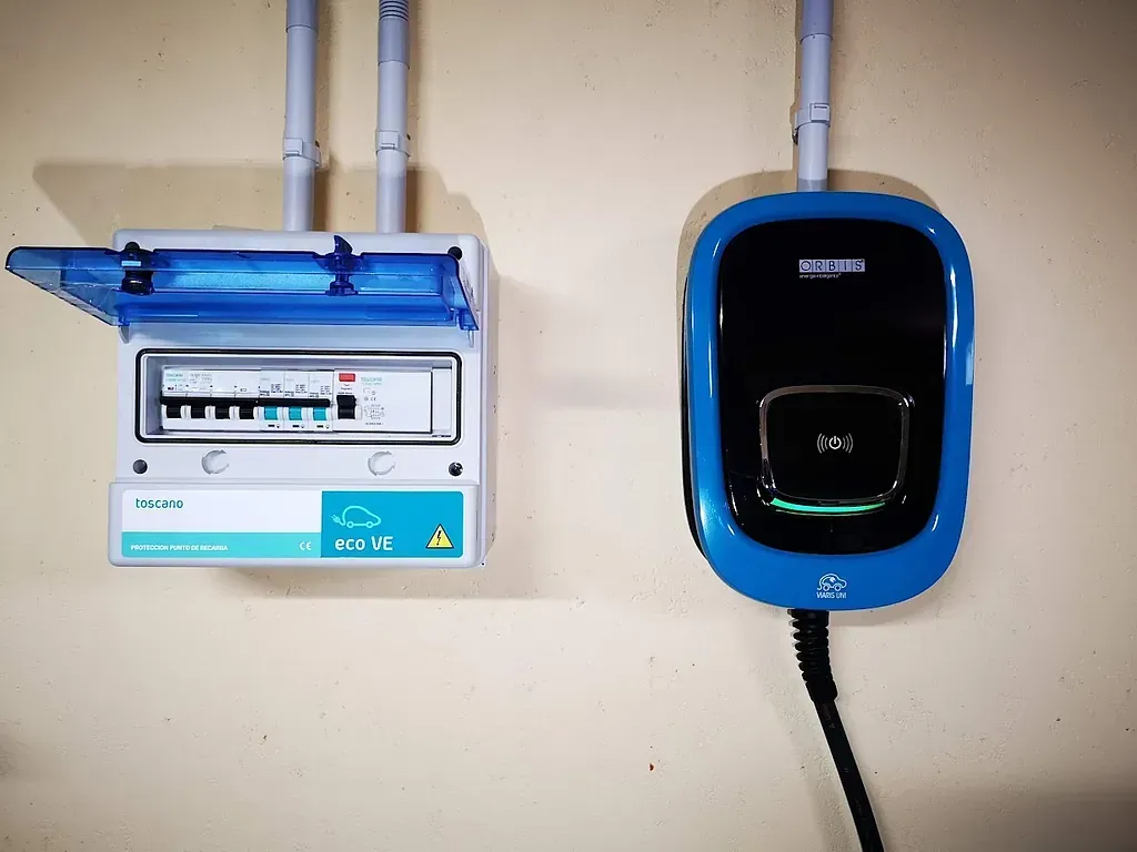 Un cargador de coche eléctrico azul está conectado a una pared al lado de un disyuntor.