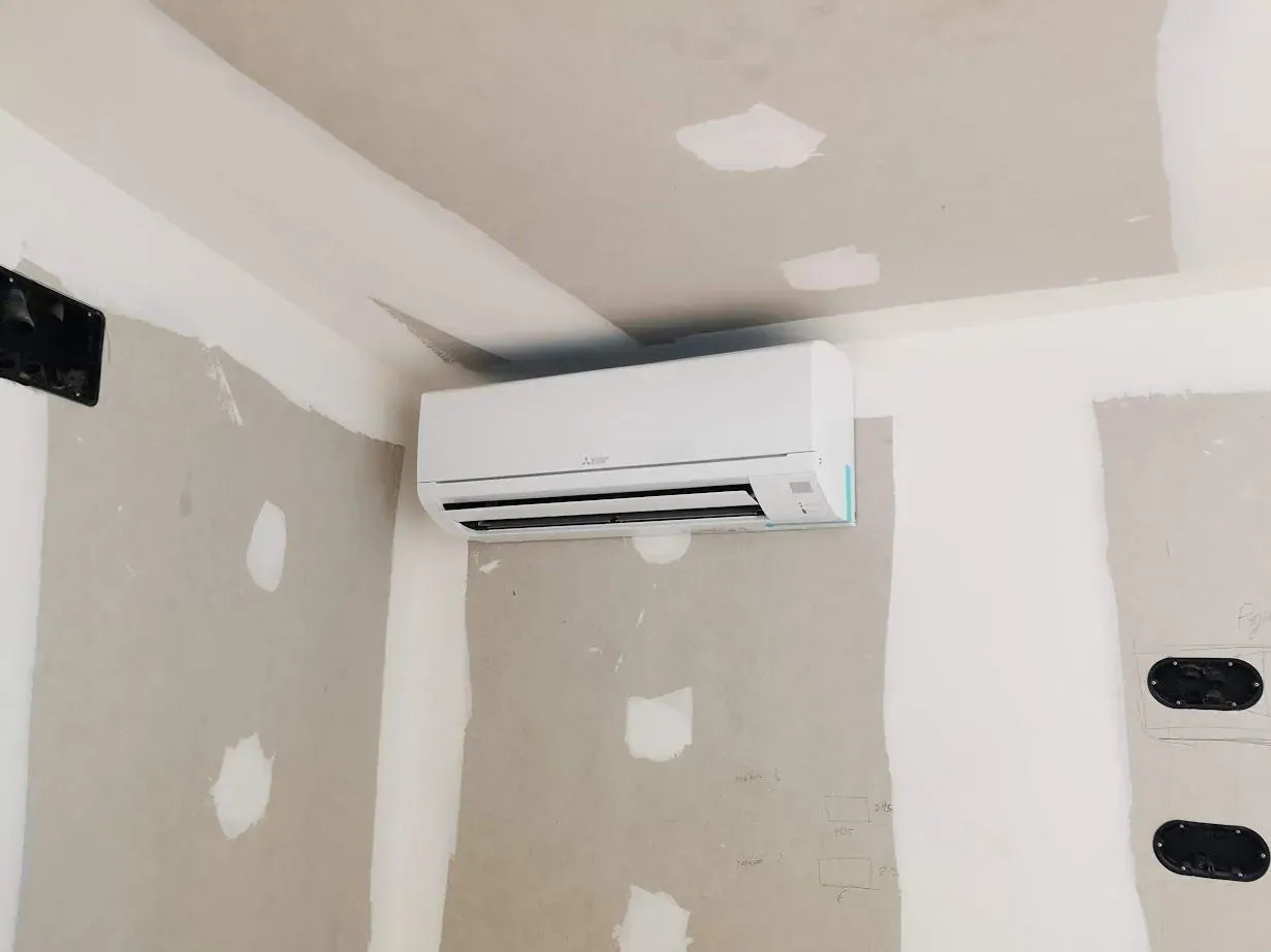 Un acondicionador de aire blanco cuelga del techo de una habitación en construcción.