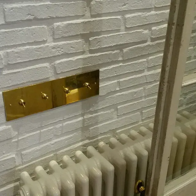 Una pared de ladrillo blanco con un radiador y un interruptor de luz.