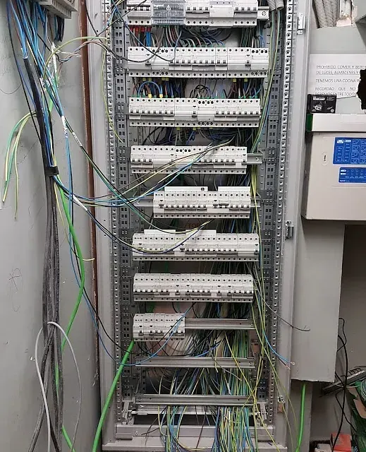 Un armario eléctrico muy desordenado con muchos cables saliendo de él.