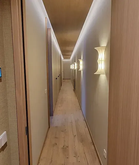 Un largo pasillo con pisos de madera y luces en las paredes.