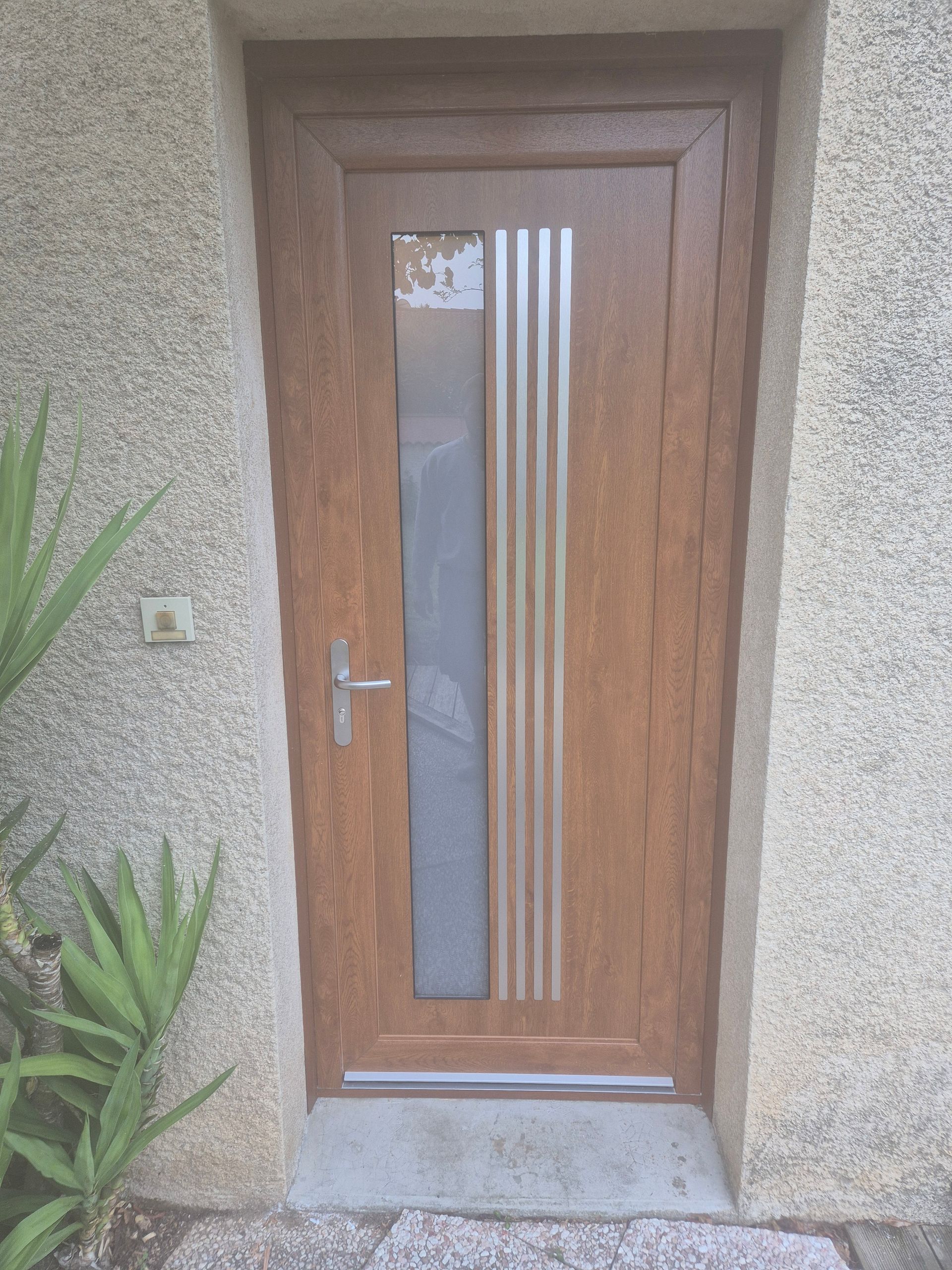 Porte d'entrée marron avec panneau de verre et accents argentés dans une porte en stuc.