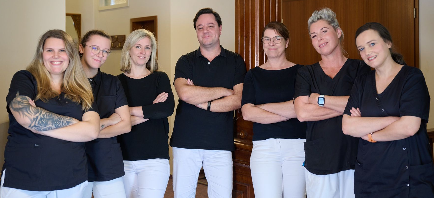 Eine Gruppe von Menschen steht mit verschränkten Armen nebeneinander.