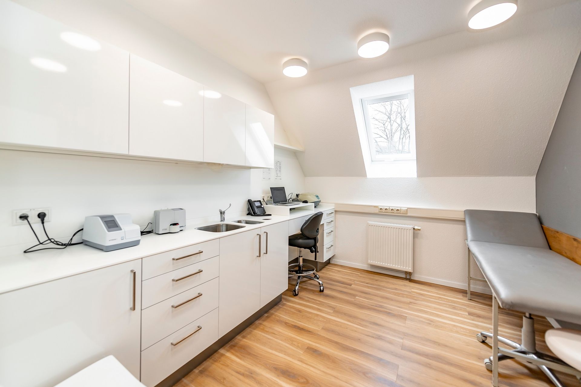 Eine Arztpraxis mit weißen Schränken, einem Schreibtisch und einer Couch.