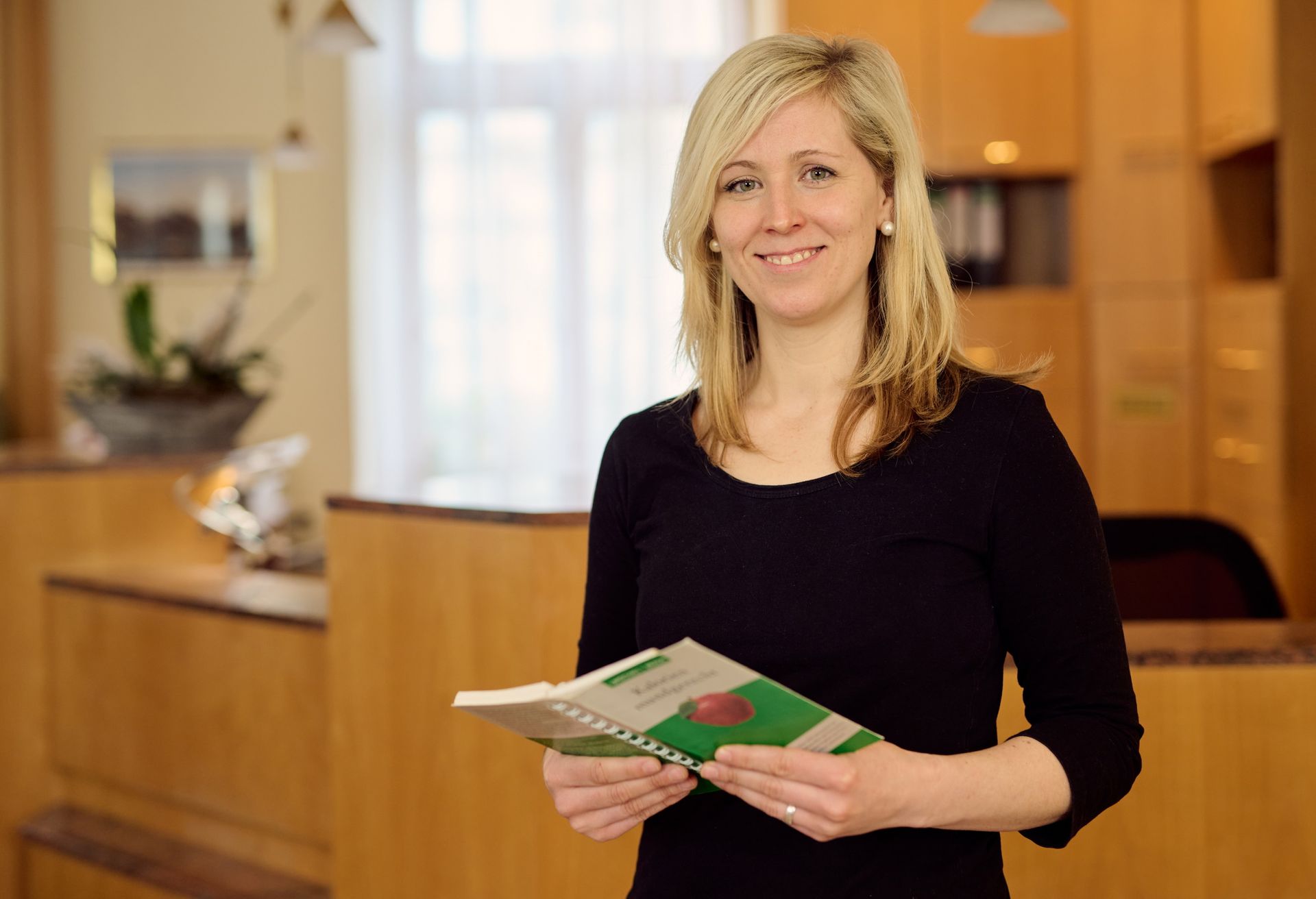 Eine Frau in einem schwarzen Hemd hält ein Buch und lächelt.