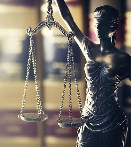 Estatua de bronce de la Dama de la Justicia sosteniendo una balanza equilibrada en un escenario de sala de tribunal difuminado.