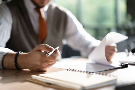 Un homme en tenue de bureau examine des documents avec un stylo et un bloc-notes sur le bureau.