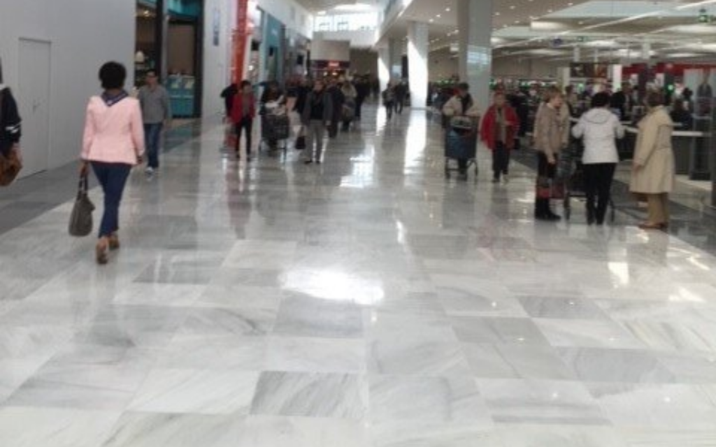 Des clients déambulent dans un centre commercial intérieur lumineux au sol en marbre brillant.
