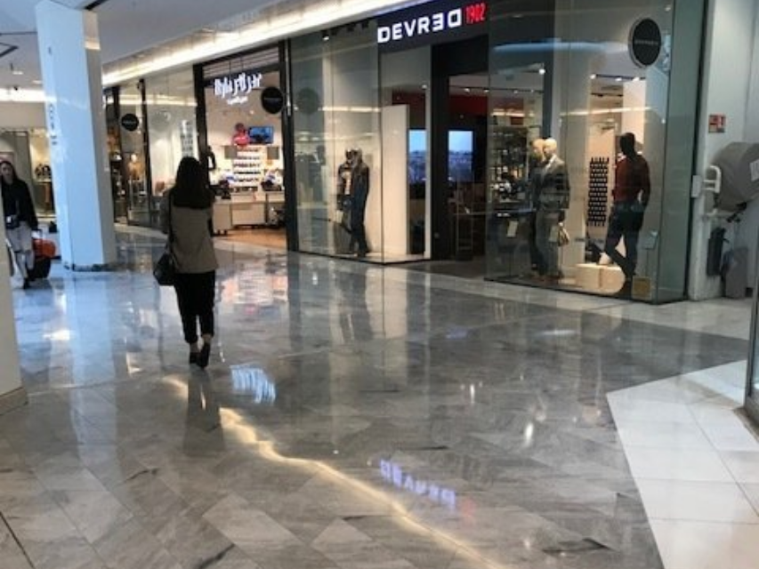 Couloir de centre commercial avec une vitrine et une personne se dirigeant vers l'entrée d'un magasin.