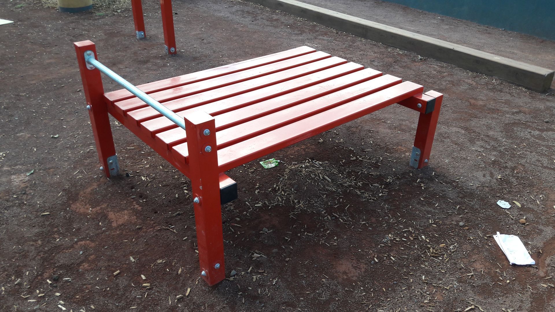 Banc en bois rouge à lattes sur un trottoir mouillé à l'extérieur