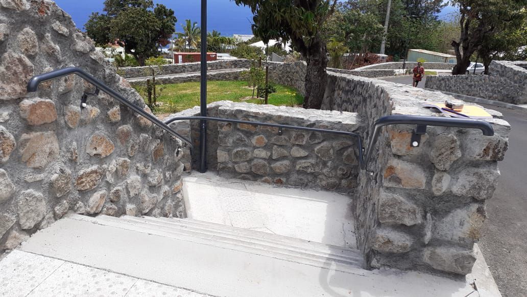 Des marches et des murets en pierre mènent à une allée dans un parc ensoleillé.