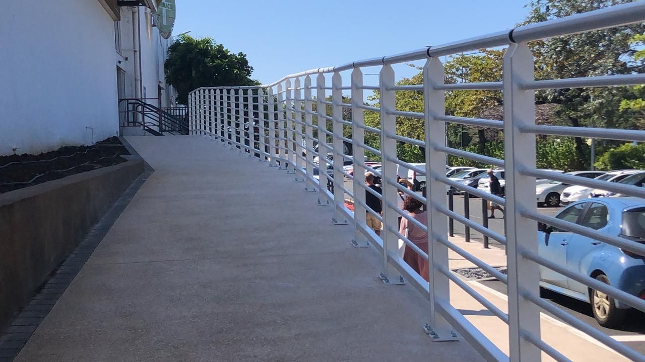 Allée piétonne en pente le long d'un bâtiment blanc, avec une rambarde métallique