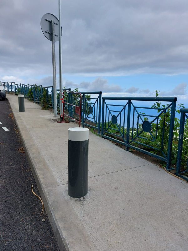 Trottoir côtier avec borne noire, rambarde métallique et ciel nuageux au-dessus de la mer
