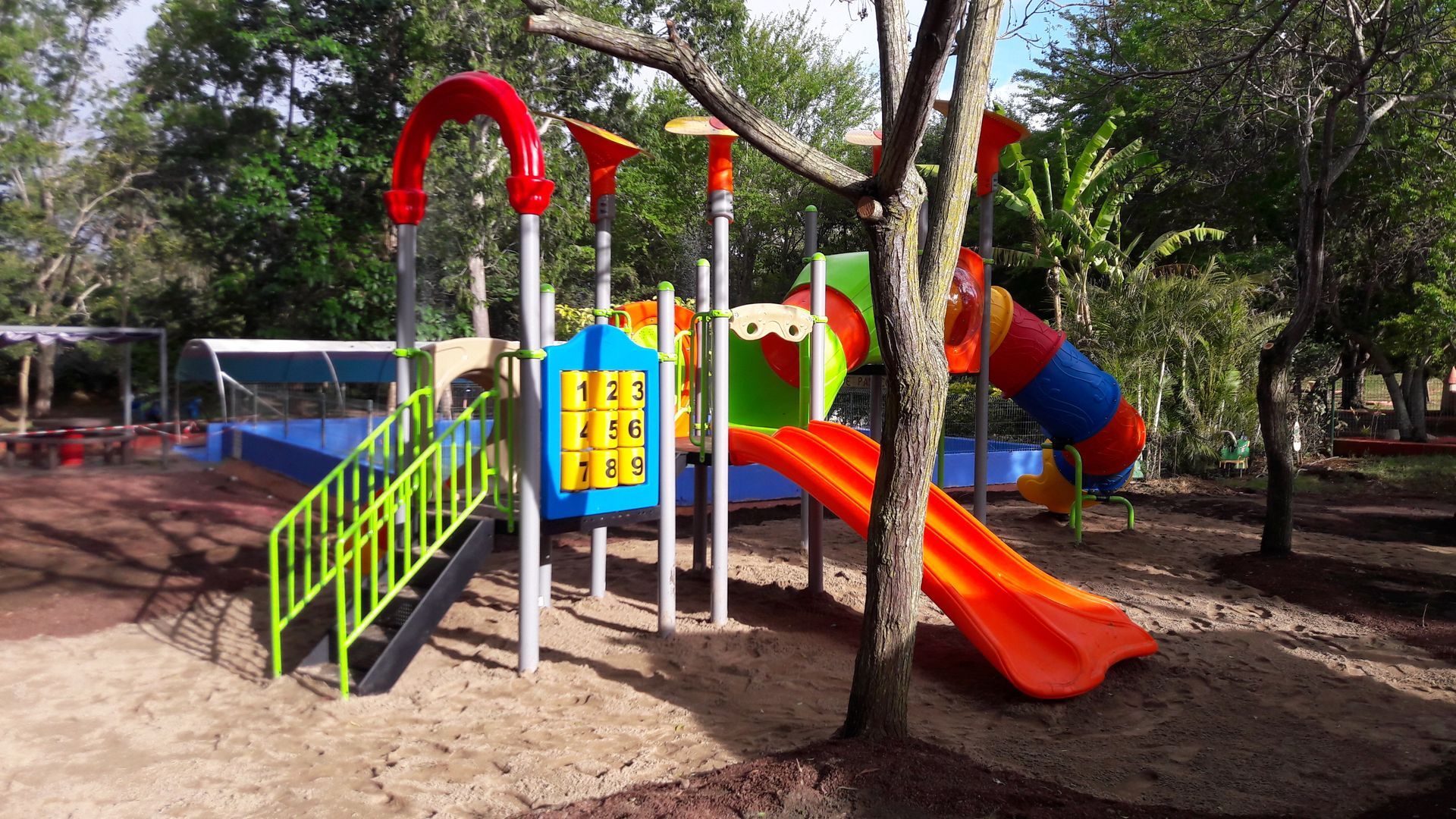 Aire de jeux colorée avec toboggans, échelles et structures d'escalade parmi les arbres sur un sol sablonneux